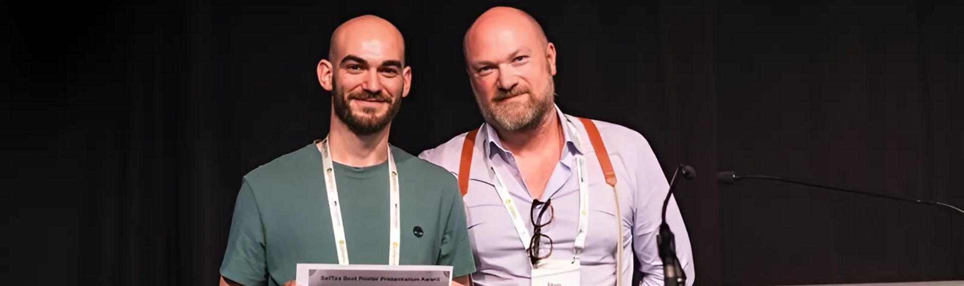 Two men standing side by side, holding a certificate in their hands.