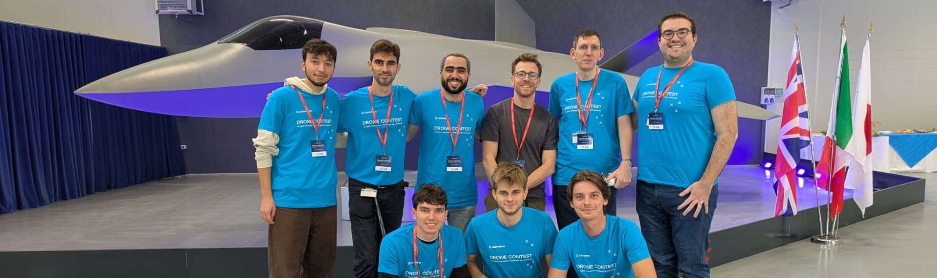 A group of people in blue shirts poses together with a drone.