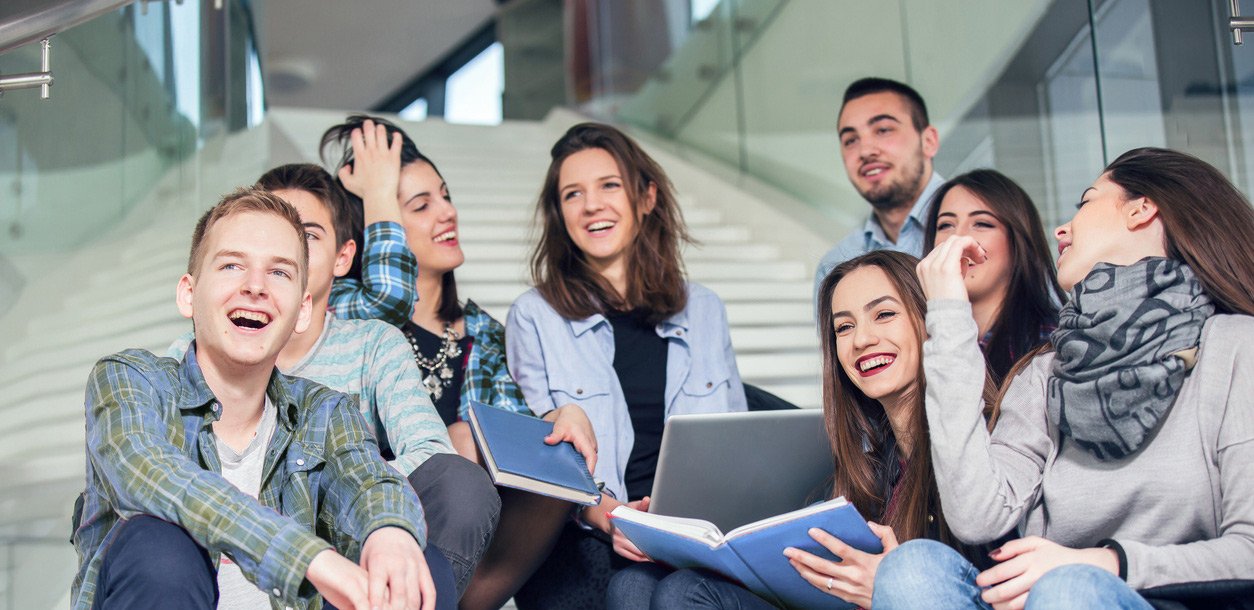 A group of young people smiling while looking at a laptop together.
