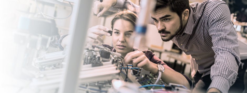 Two people, a woman and a man, working together on technical equipment in a laboratory, focused on electronic and mechanical components.
